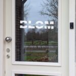 Een voordeur met op het glas een opdruk van de achternaam onderbroken door een horizontale lijn met daarop de voornamen in sierlijk lettertype