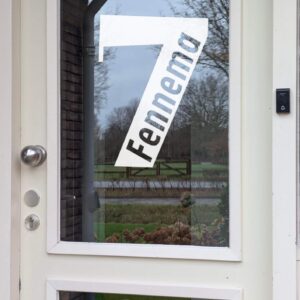 Een voordeur met op het glas een opdruk van een groot cijfer met daarin de achternaam geschreven