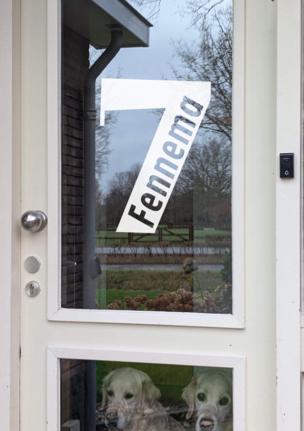 Een voordeur met op het glas een opdruk van een groot cijfer met daarin de achternaam geschreven