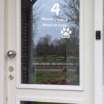 Voordeur met op het glas een opdruk van een cirkel van stippen en een dierenpoot met een naam, in het midden staat het huisnummer en de namen.