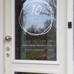Voordeur met op het glas een opdruk van twee in elkaar overlopende getekende cirkels met in het midden de naam in sierlijk lettertype