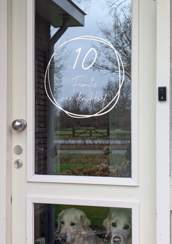 Voordeur met op het glas een opdruk van twee in elkaar overlopende getekende cirkels met in het midden de naam in sierlijk lettertype