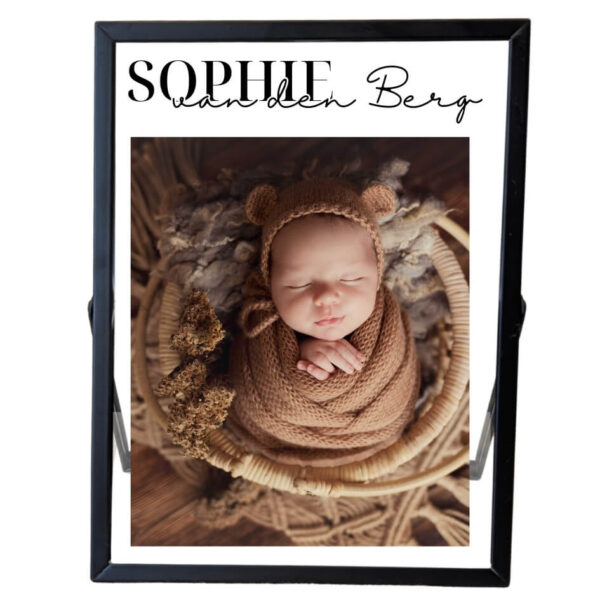Een zwart fotolijstje met daarin een foto van een baby met een opdruk van de voornaam met daaronder de achternaam in sierlijke letters.