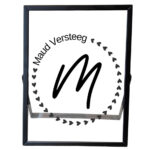 Een zwarte fotolijst met een cirkel van hartjes, die links bovenin onderbroken wordt door de naam. In het midden staat een sierlijk initiaal.