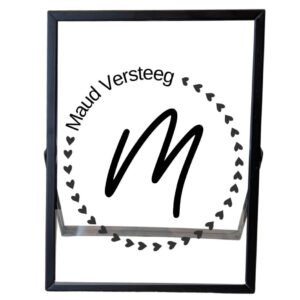 Een zwarte fotolijst met een cirkel van hartjes, die links bovenin onderbroken wordt door de naam. In het midden staat een sierlijk initiaal.