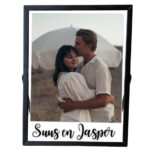 Een zwarte fotolijst met daarin een foto van een verliefd stel met daaronder een opdruk van twee namen.