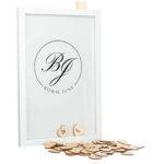 Een witte staande fotolijst met een zwarte opdruk van een cirkel met daarin sierlijke initialen en de volledige namen