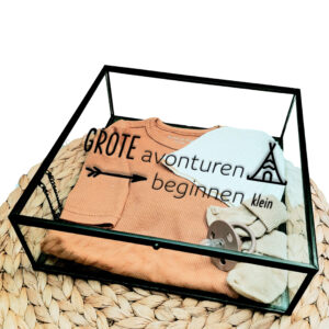 Vierkant glazen kistje met zwart frame en bedrukking van een tipitent, een pijl en de tekst: grote avonturen beginnen klein