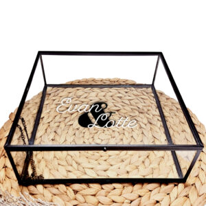 Vierkant glazen kistje met zwart frame en een sierlijke bedrukking van twee witte namen met daartussen een zwart en teken.