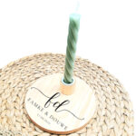 Ronde blanco houten kaarsenstandaard met een zwarte opdruk van sierlijk in elkaar overlopende initialen met daaronder de namen en de datum