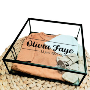 Vierkant glazen kistje met zwart frame en bedrukking van de naam tussen twee lijnen, de onderste lijn is onderbroken door de geboortedatum.