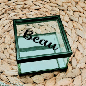 Glazen kistje met zwart frame en een zwarte opdruk van een naam in sierlijke letters geschreven.