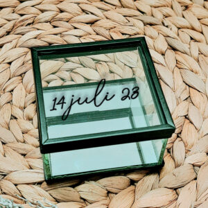 Vierkant glazen kistje met zwart frame en een opdruk van een datum in sierlijke letters geschreven.