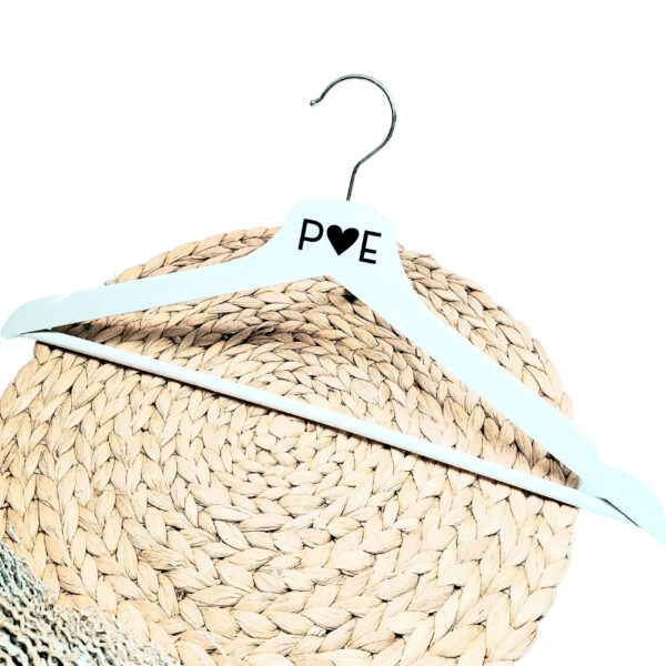 Een wit houten kleerhanger met daarop de bedrukking van de initialen met een hartje er tussen.