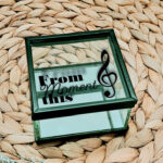 Vierkant glazen kistje met zwart frame en een opdruk van een muzieksleutel met tekst: from this moment, waarvan moment in sierlijk lettertype