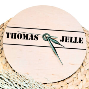 Een blanco houten ronde klok met zwarte wijzers en een opdruk van twee namen in stoere letters met daar boven en onder een lijn.