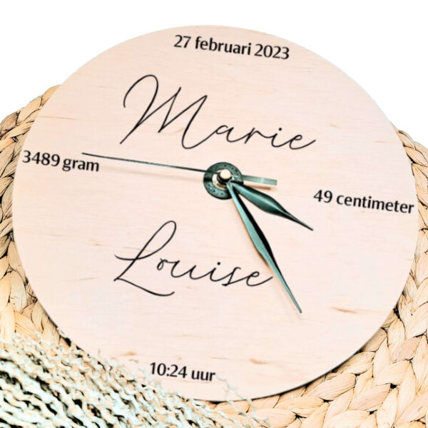Een blanco houten ronde klok met zwarte wijzers en een opdruk van de naam in sierlijke letters met daaromheen de datum tijd lengte en gewicht