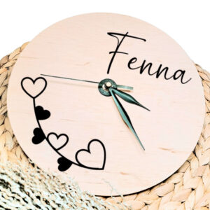Een blanco houten ronde klok met zwarte wijzers en een opdruk van de naam rechts bovenin en een takje met hartjes linksonder.