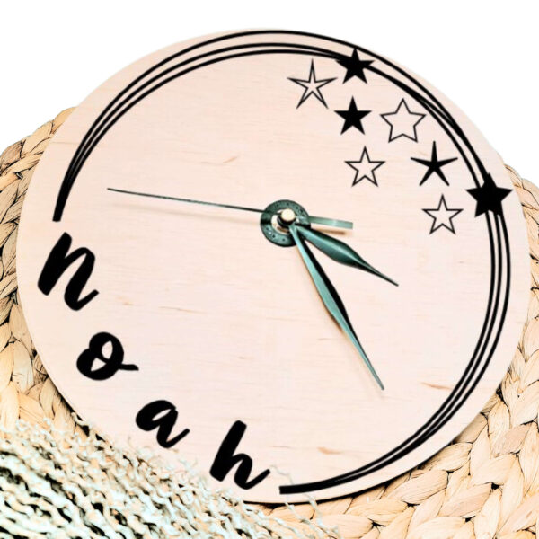 Een blanco houten ronde klok met zwarte wijzers en een opdruk van diverse speelse cirkels welke onderbroken worden door de naam en sterren.