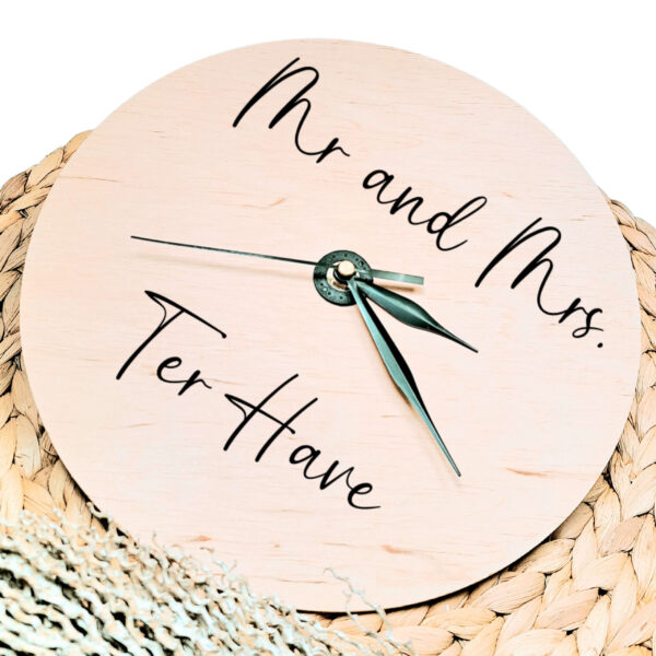 Een blanco houten ronde klok met zwarte wijzers en een opdruk van mr. and mrs. met daaronder de achternaam.