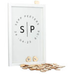 Een witte staande fotolijst met een zwarte opdruk van de initialen met daar omheen een cirkel van de volledige namen, datum en tijd.