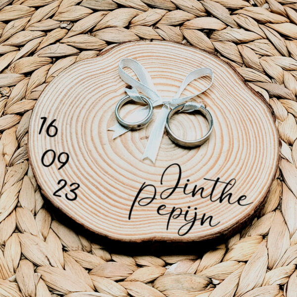 Rond ringplankje gemaakt van een boomstamschijf met daarop 2 ringen aan een satijnen lint en een sierlijke zwarte opdruk van de namen en datum.