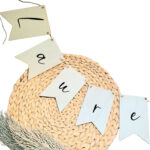 Blanco houten vlaggetjes aan een jute touw met op elk vlaggetje een zwarte sierlijke letter.