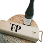 Houten rechthoekige wijnkist met touw als handvat met zwart opdruk van 2 initialen met daarin verticaal de namen.